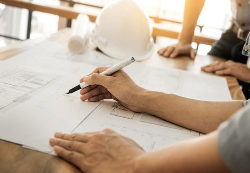 Architects engineer discussing at the table with blueprint - Clo Basement Architects & Construction